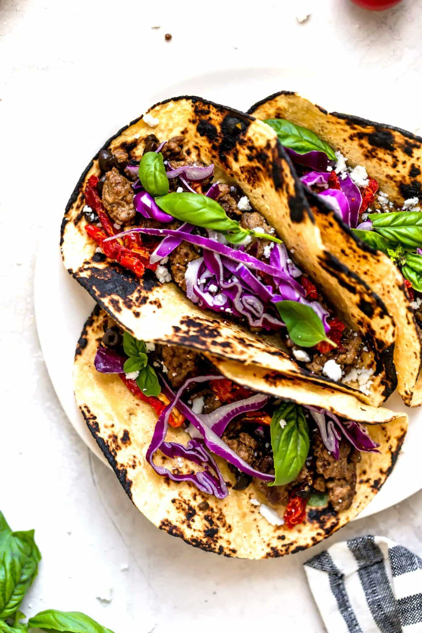 Three lamb tacos served in charred tortillas topped with purple cabbage