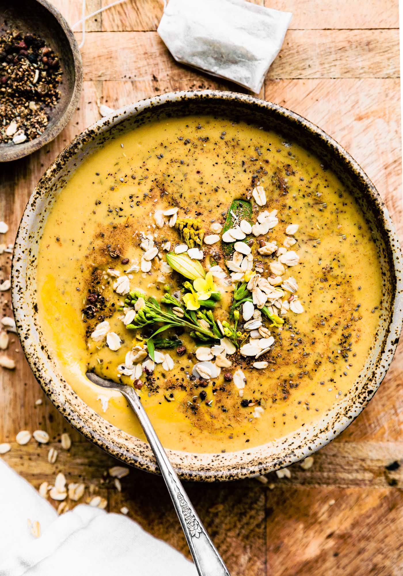 Overhead view chai turmeric smoothie in speckled brown bowl topped with old-fashioned rolled oats and small flowers.