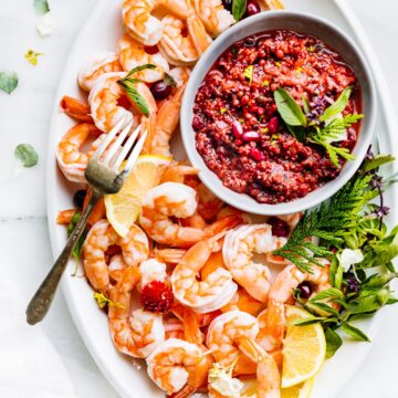 Overhead view white platter filled with shrimp and small bowl filled with cranberry basil cocktail sauce.