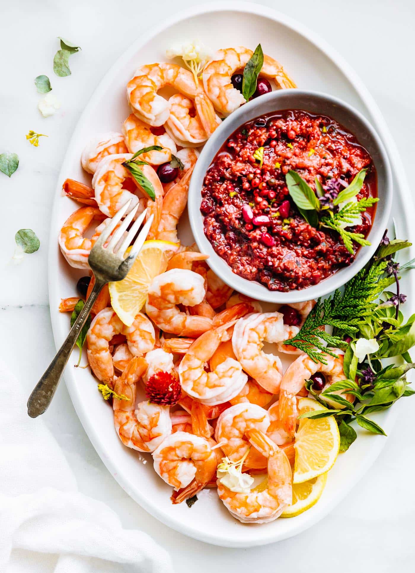 Overhead view white platter with shrimp, small bowl filled with cranberry basil cocktail dipping sauce.
