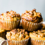 Side view several spiced pear muffins with nut topping stacked up on each other on a white serving tray.