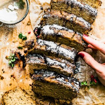 A hand removing a slice of Irish cream banana bread from a cut loaf on a wooden cutting board.