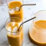 two glasses with metal straws and a pitcher of Thai iced coffee sitting on a marble countertop