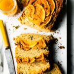 Overhead view orange zucchini bread with several thick slices cut from loaf on white cutting board