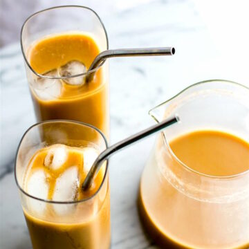 two glasses with metal straws and a pitcher of Thai iced coffee sitting on a marble countertop