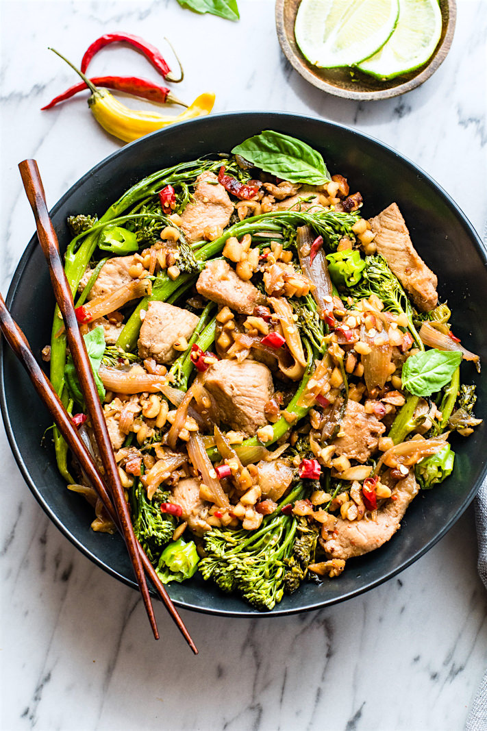An overhead view of  Thai style pork broccolini stir fry in a  bowl with chopsticks.