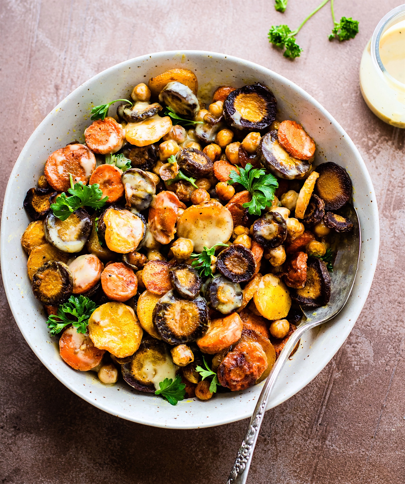Turmeric Roasted Chickpea Carrot Salad served in a speckled serving bowl drizzled with tahini-apple cider vinegar dressing.