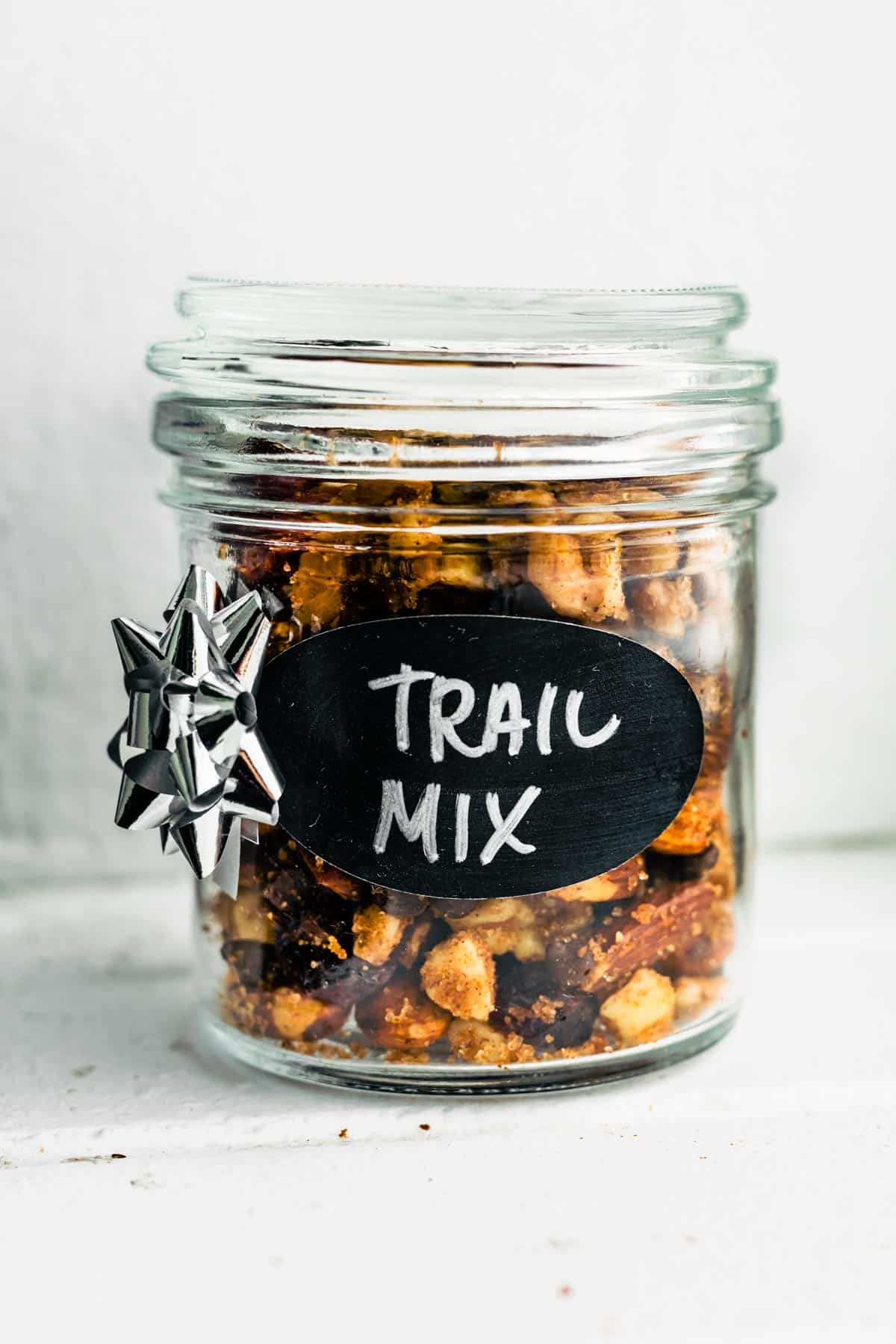 Glass jar filled with pumpkin spice trail mix, labeled “Trail Mix” with a small silver gift bow on the side.