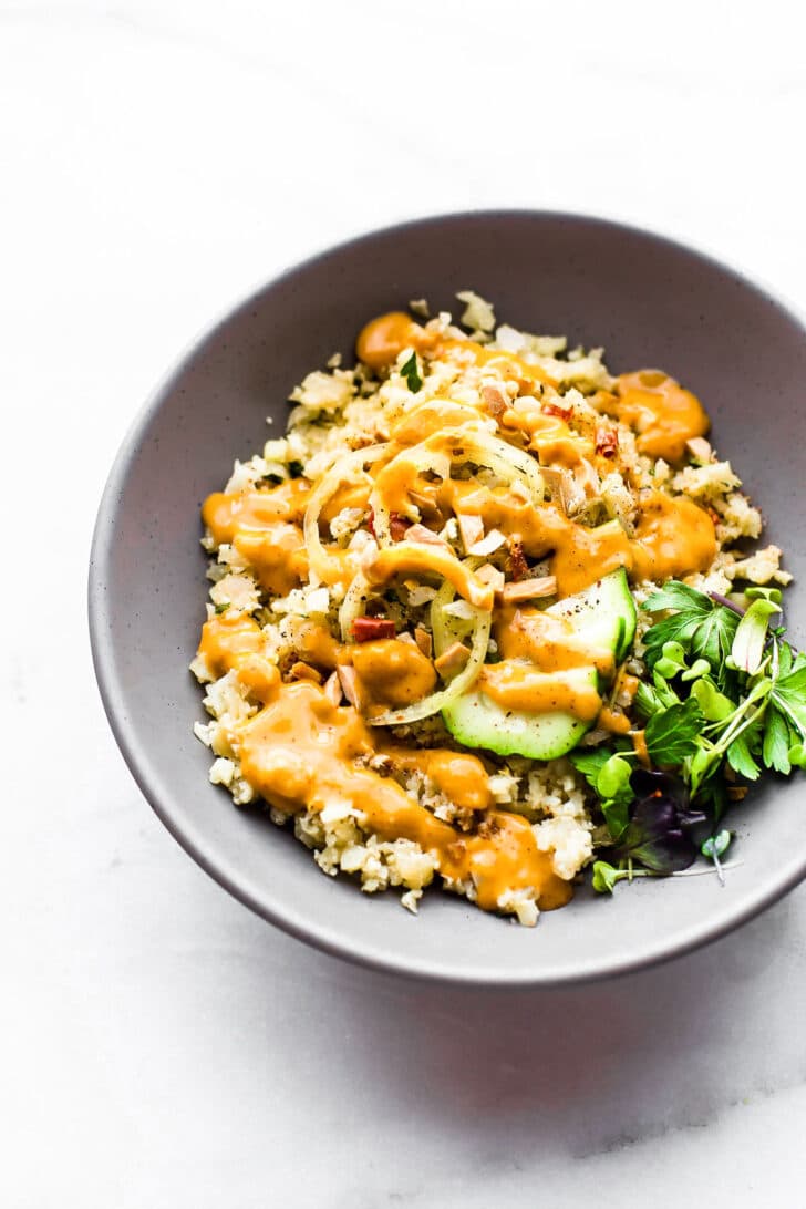Chili garlic cauliflower risotto served in bowl topped with orange sauce.