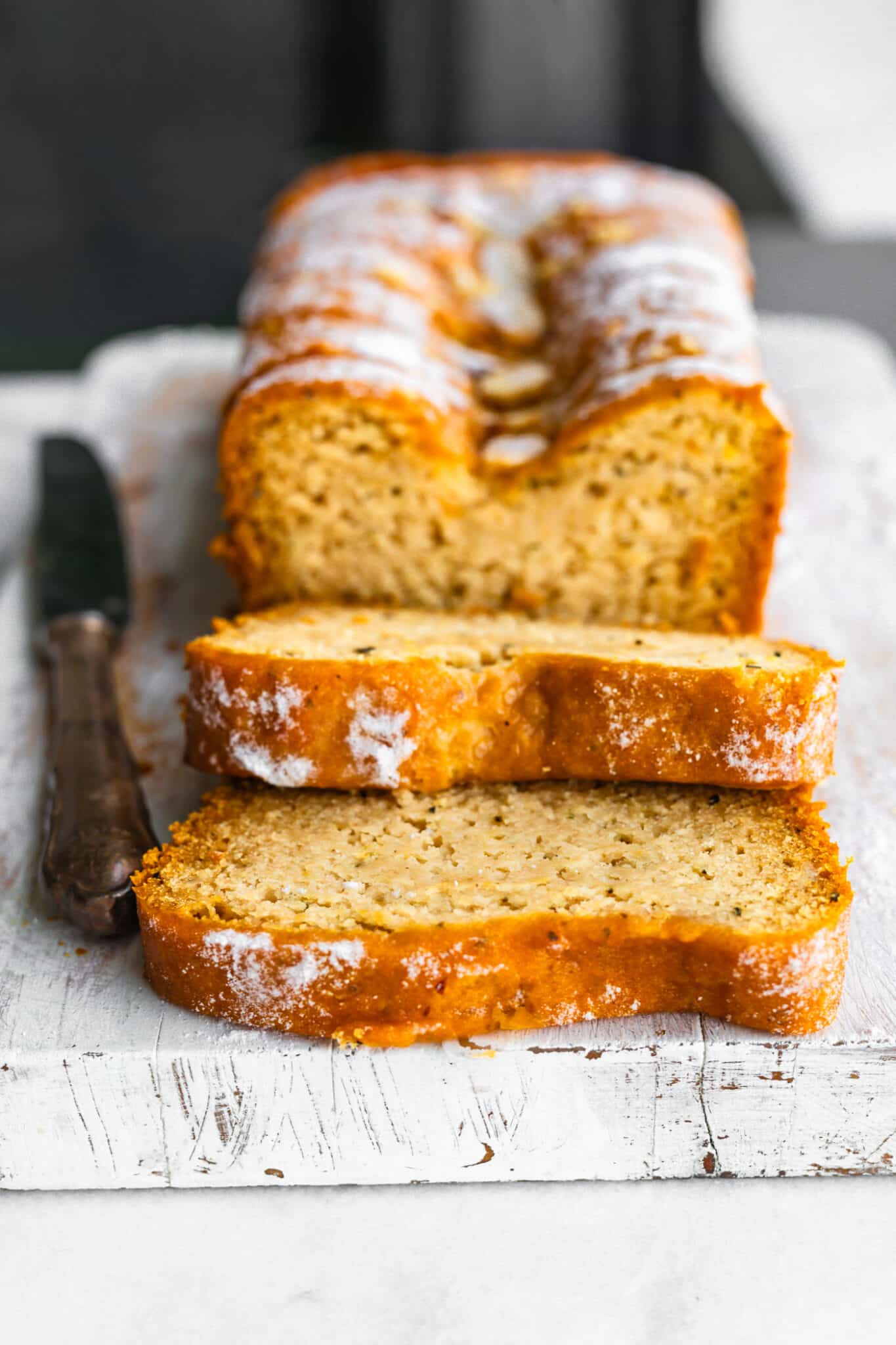Close-up of sliced gluten-free Earl Grey tea cake with golden crust and light powdereding sugar and citrus glaze