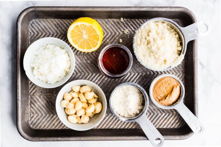 coocnut flour, almond butter, lemon, maple syrup, coocnut, and macadamia nuts on a sheet pan