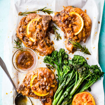 Marmalade Pork Chops and broccolini sitting on a parchment paper covered sheet pan