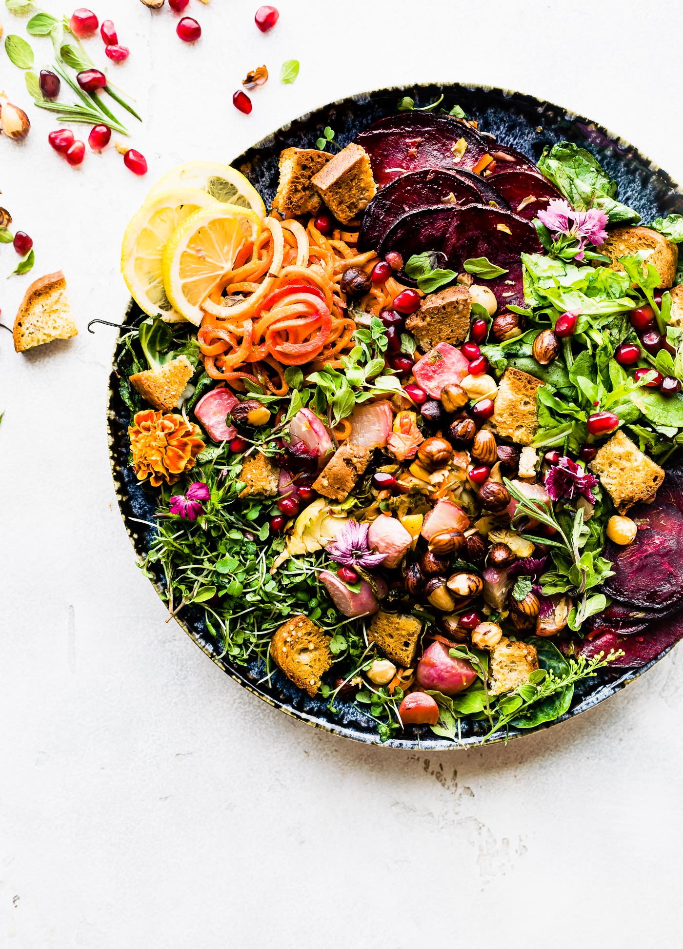Overhead view herb roasted vegetable panzanella salad on dark stone plate.