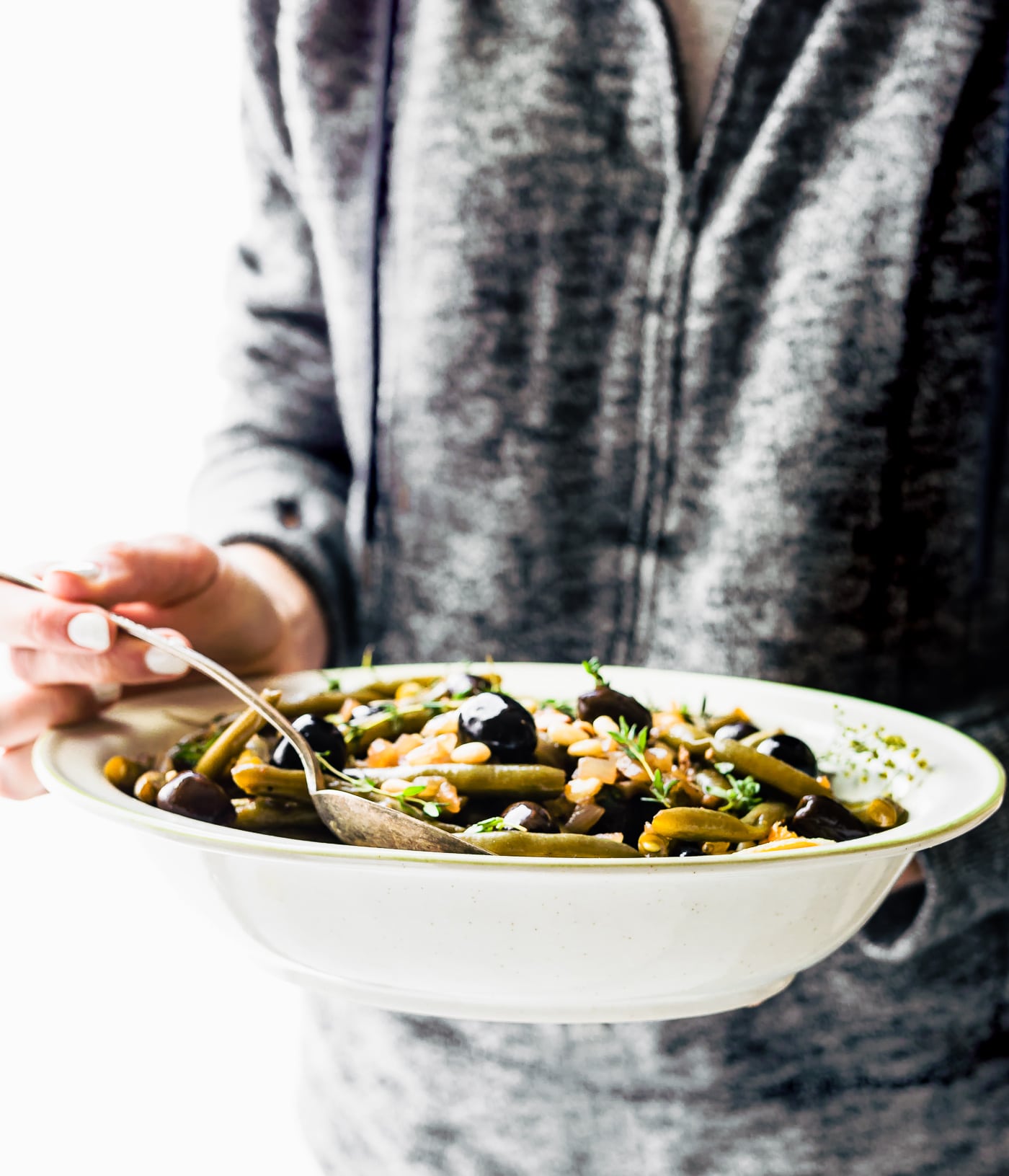 Balsamic olive oil braised olive oil in white serving dish being held with two hands.