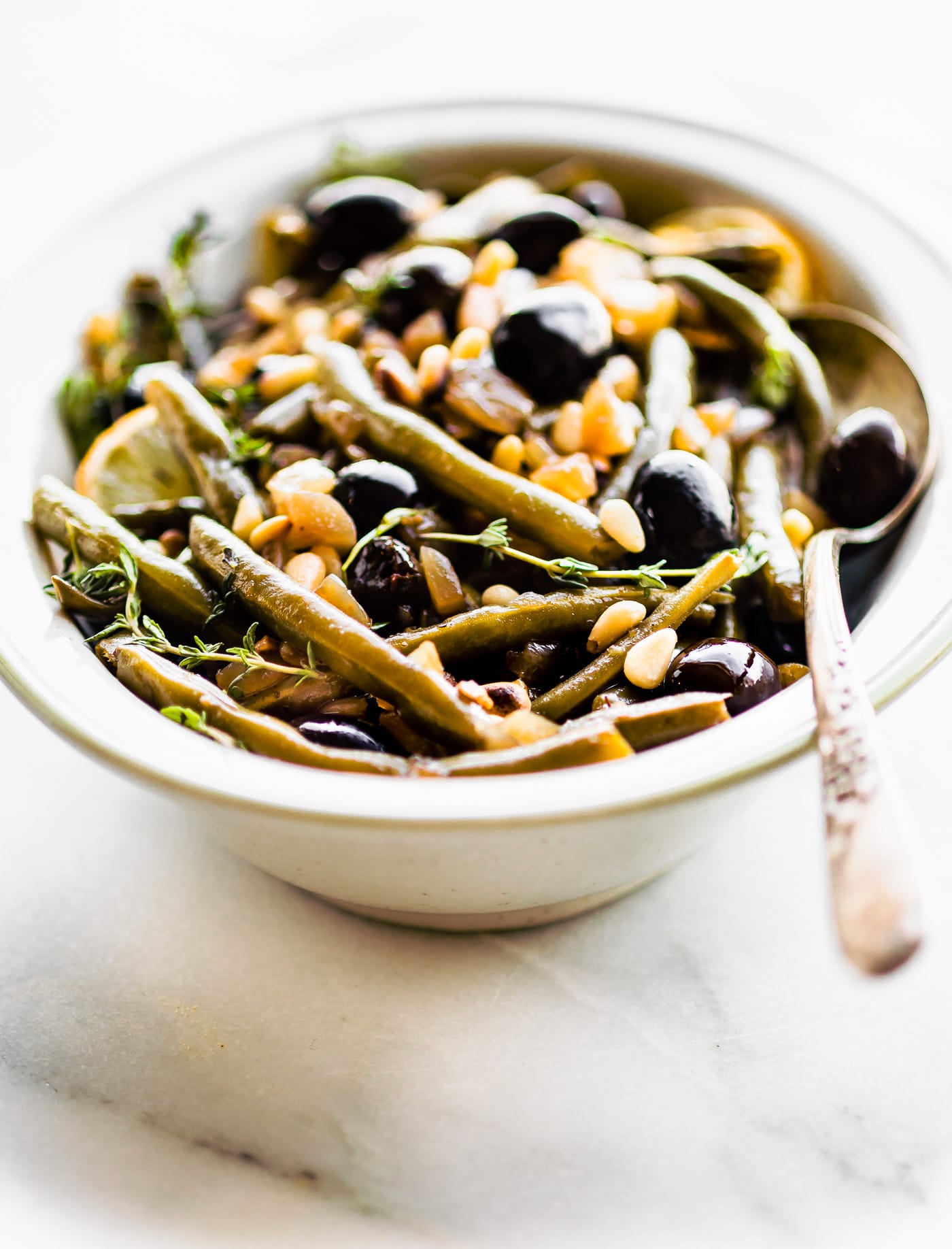 Side view balsamic olive oil braised green beans with olives in white serving dish.