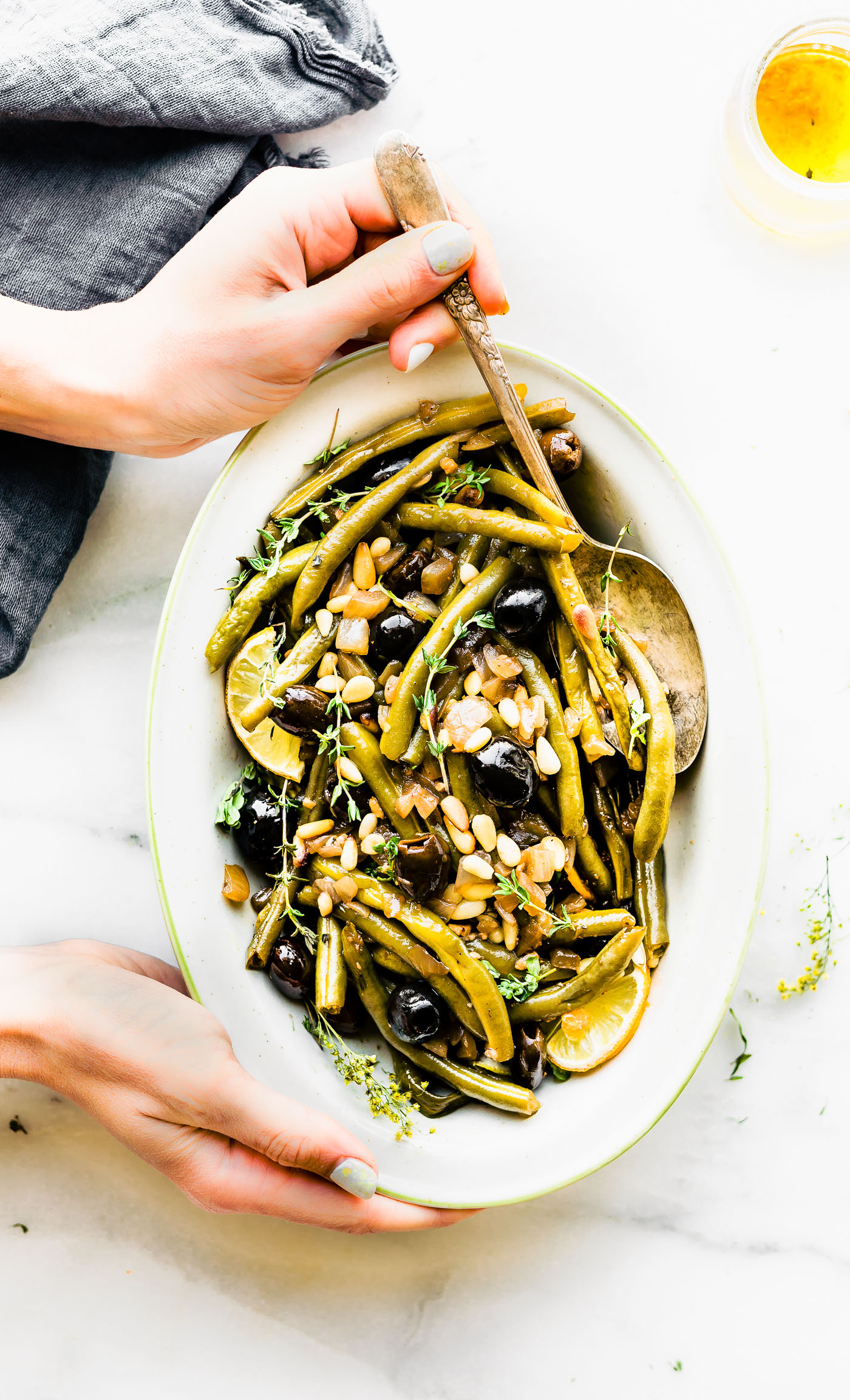 Balsamic braised green Beans in white oval serving dish being held with two hands.