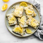 Overhead view several lemon coconut energy bars topped with lemon slices on plate.