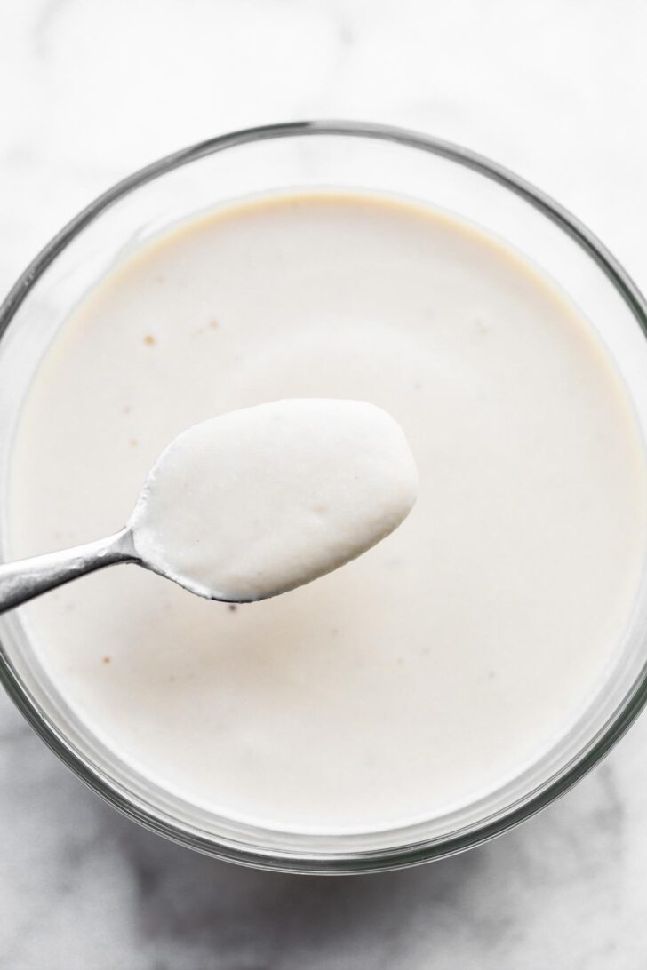A spoon dripping off cashew cream sauce into a bowl