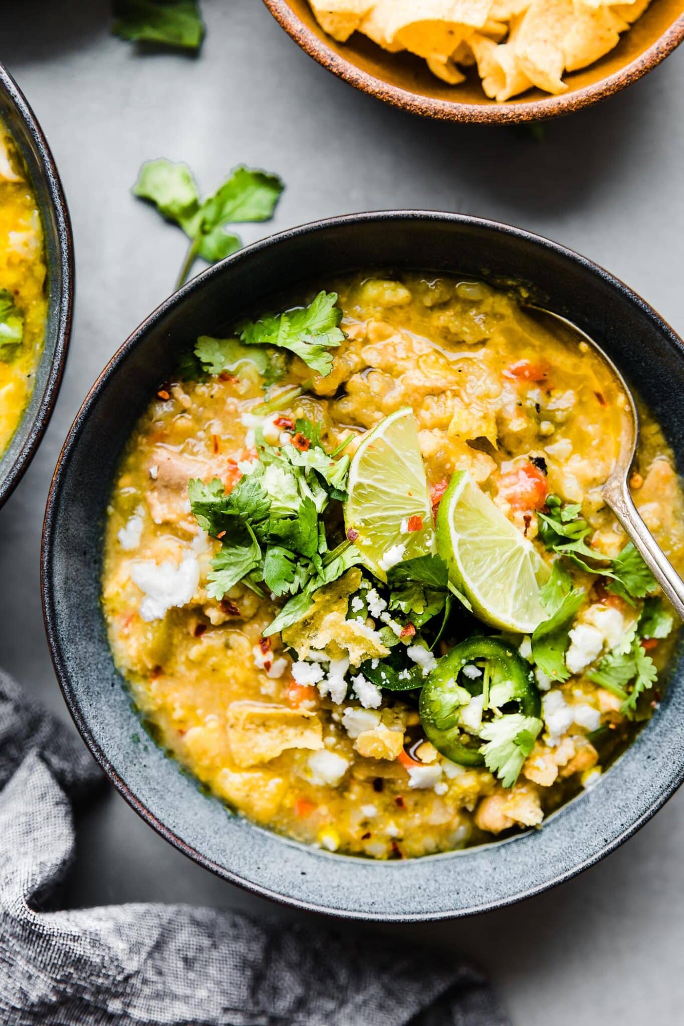Beanless Tortilla Chicken Verde Chili served in a dark grey bowl with a spoon in the soup, topped with lime wedges and fresh cilantro.
