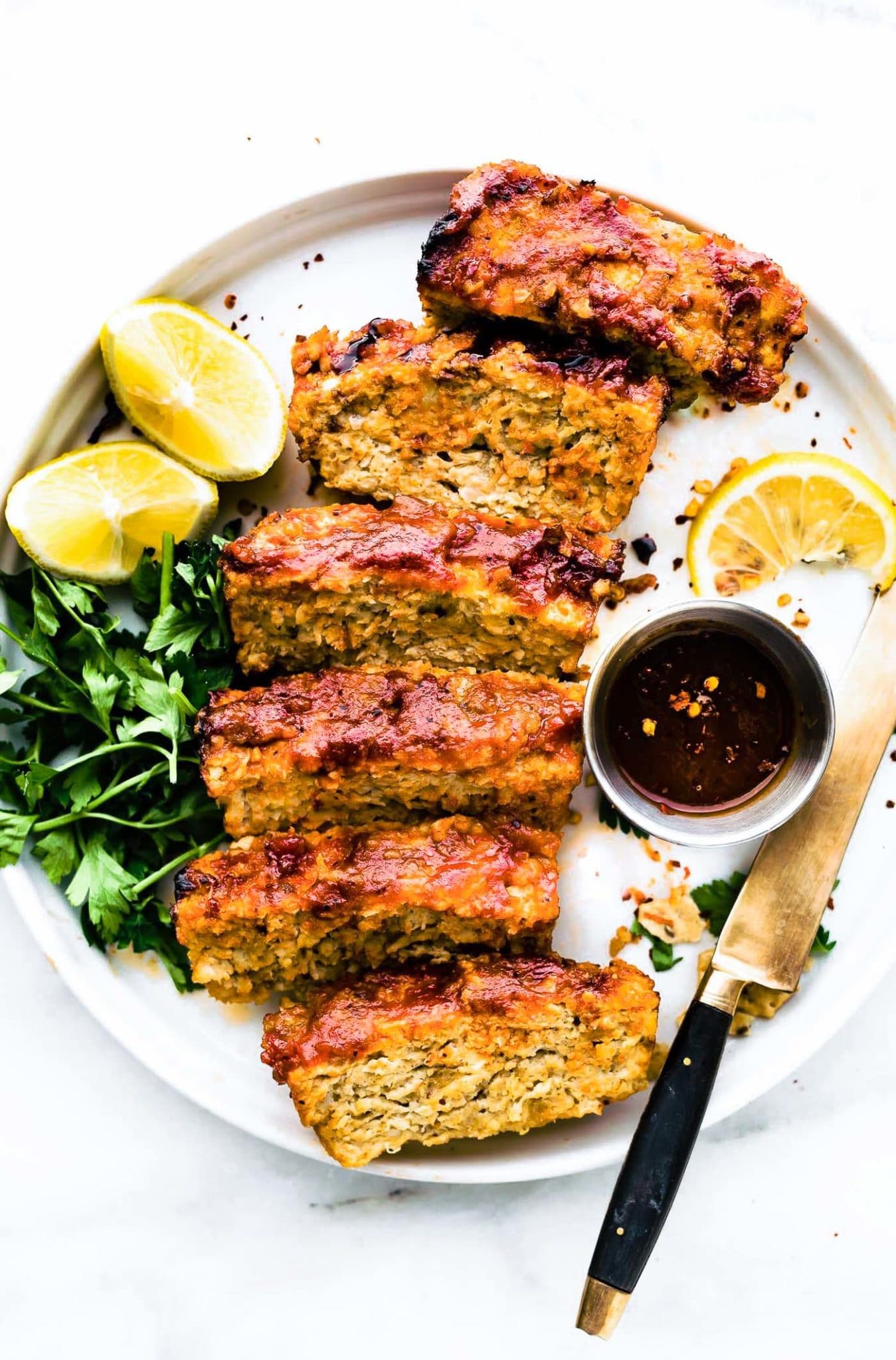 slices of glazed BBQ meatloaf plated on white plate with sauce on side.