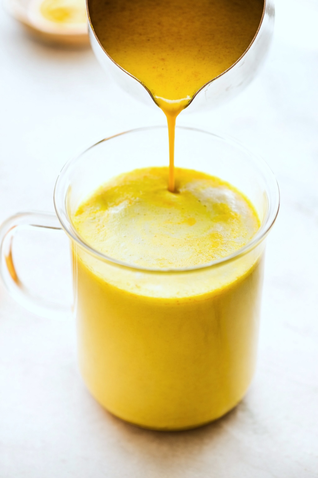 Pour shot of golden turmeric latte being poured into glass mug