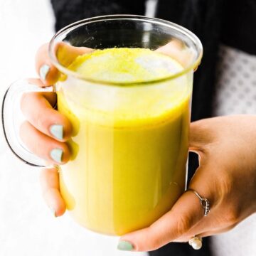woman holding a clear mug of blood orange turmeric tea latte