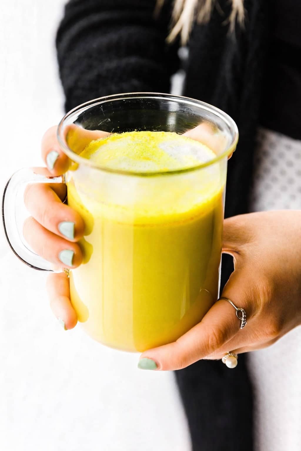 woman holding a clear mug of blood orange turmeric tea latte