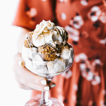 A woman holding a pedestal glass filled with cinnamon cake bites coated in white chocolate topped with ice cream.
