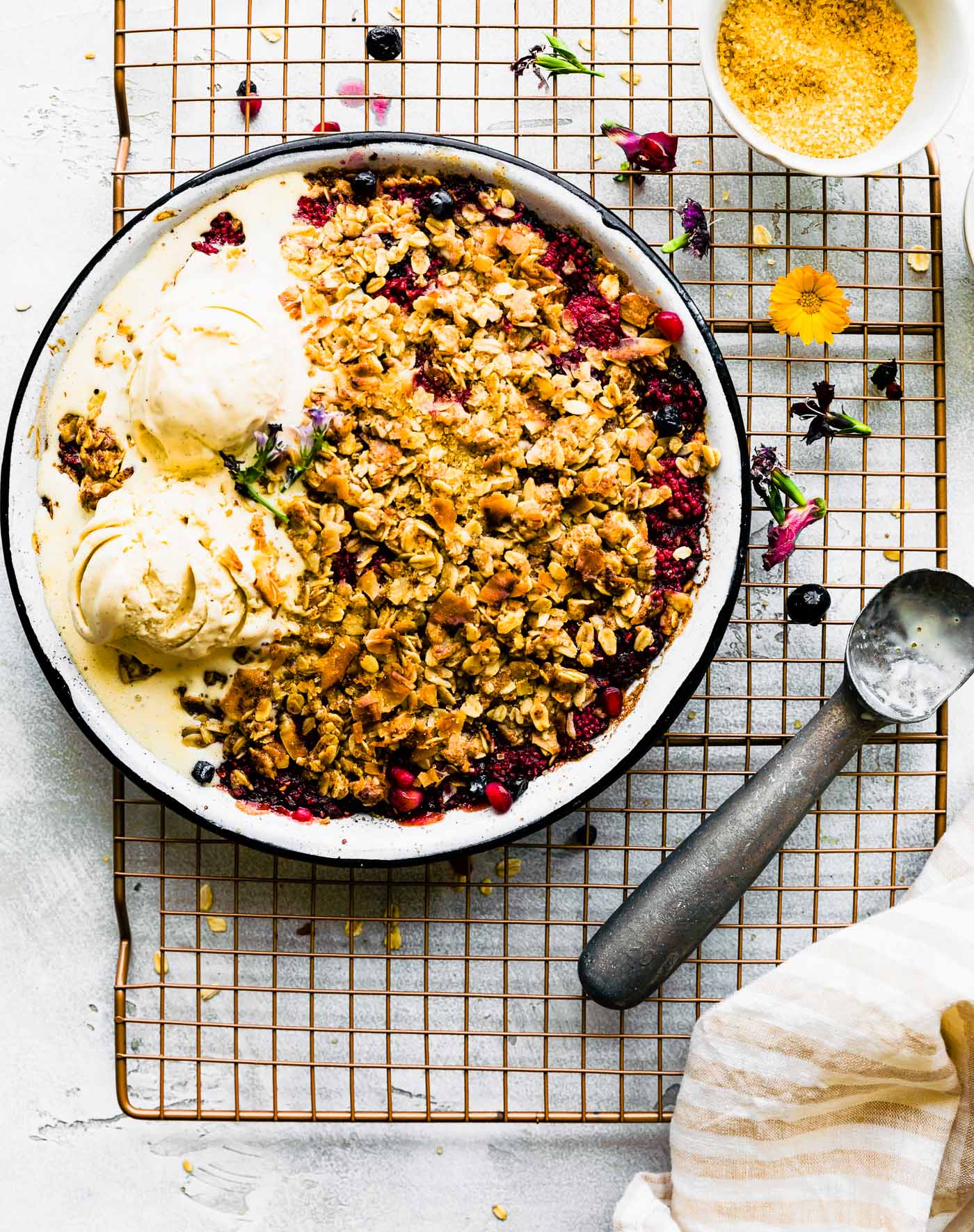 Overhead view pie plate filled with coconut summer berry crisp, two scoops of melting ice cream on one side of crisp.