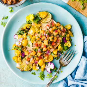 Blue plate with serving of baked salmon fillet topped with chipotle peach salsa and fresh cilantro.