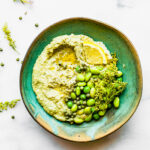 vegan edamame pesto dip in green bowl topped with shelled edamame and lemon slices.