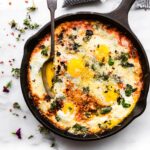 Italian egg bake prepared in a cast iron skillet. A large spoon is scooping out a serving from the skillet