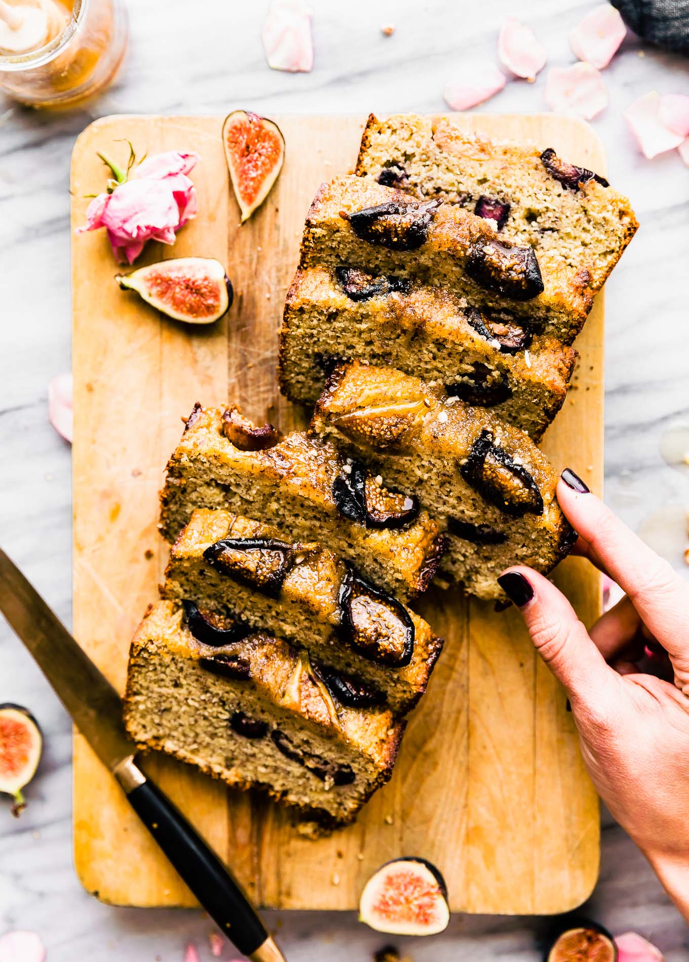 Almond flour loaf cake with roasted figs on top cut into thick slices on cutting board.