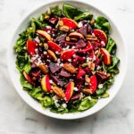 chopped apple and marinated beet salad in a white bowl with nuts on top