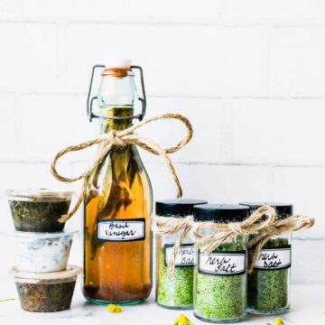 Tall glass jar, bottles and small containers filled with preserved herbs.