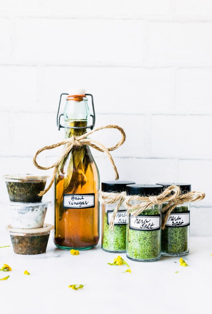 Tall glass jar, bottles and small containers filled with preserved herbs.