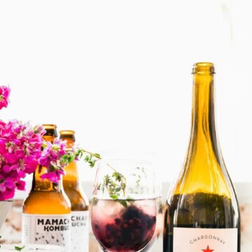 Bottles of wine, glasses of drinks, and floral arrangements on white table.