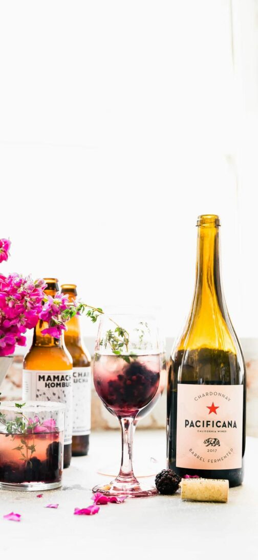 Bottles of wine, glasses of drinks, and floral arrangements on white table.