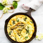 Overhead view small cast iron skillet with pumpkin frittata, topped with fresh herbs and spinach.