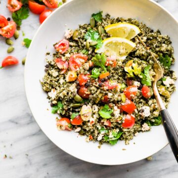 Greek cauliflower rice pilaf served in white bowl topped with cherry tomatoes and lemon slices.