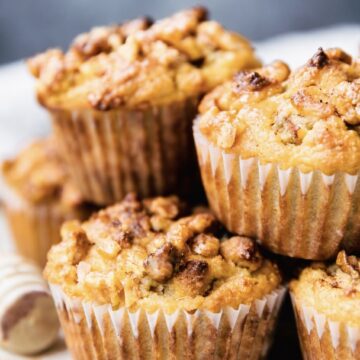 Close-up of nutty-streusel pear muffins on a white plate, with the front muffin in sharp focus and a soft blurred background.