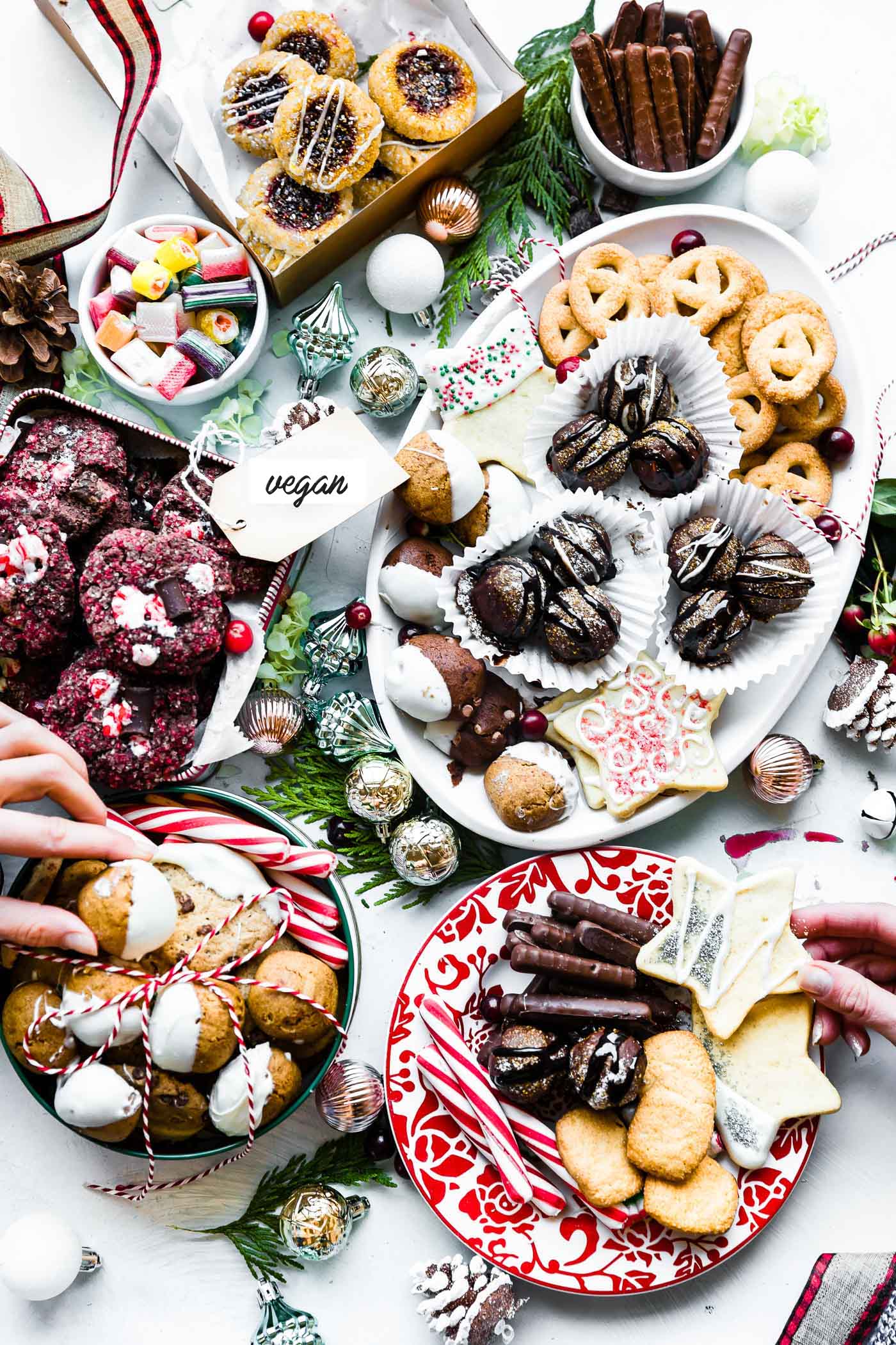 Overhead view white platter, cookie box, and small bowls filled with assortment of vegan Christmas cookies