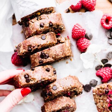A hand removing a slice of edible cookie dough with raspberries and chocolate chips from a loaf of cookie dough.