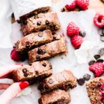 A hand removing a thick slice of raspberry chocolate chip edible cookie dough from a loaf of cookie dough.