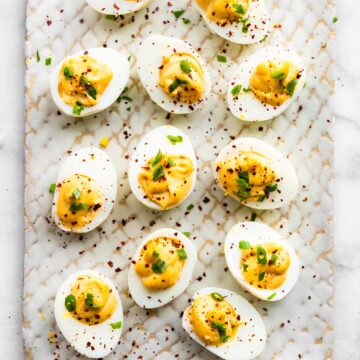 White platter filled with spicy chipotle deviled eggs topped with fresh herbs.