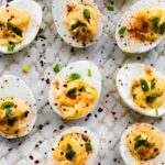 chipotle deviled eggs topped with cilantro and paprika, arranged on a white serving plate.