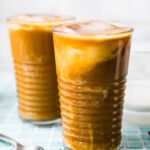 Two tall clear glasses filled with iced coffee latte