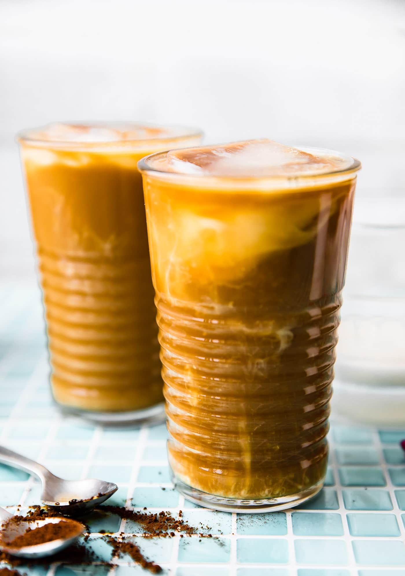 Two tall clear glasses filled with iced coffee latte
