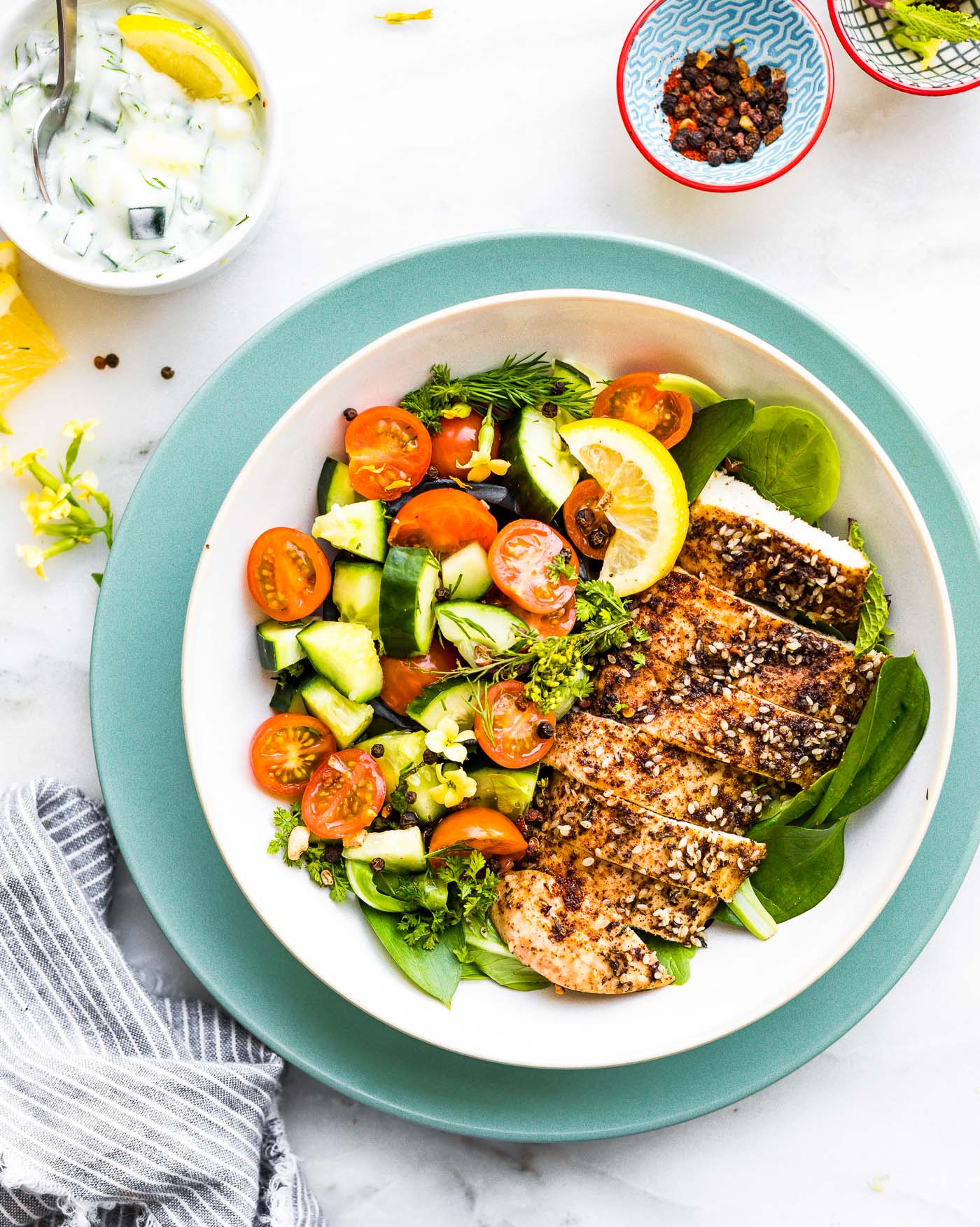 Turquoise rimmed bowl filled with Za'atar Chicken Bowls with Tomato and Cucumber Raita, topped with fresh herbs