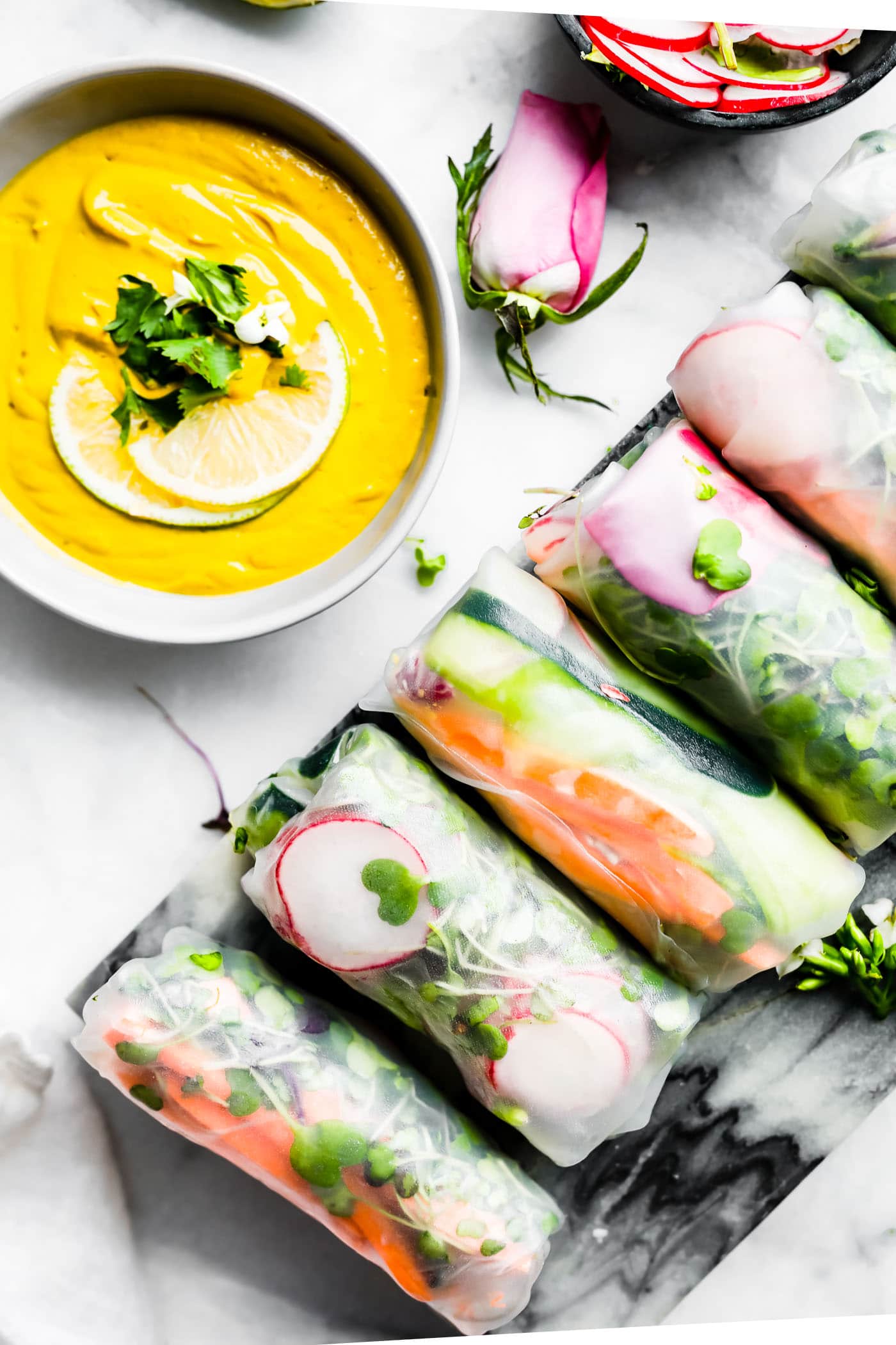 Overhead view several spring rolls lined up on black cutting board with bowl of curry dipping sauce on the side.